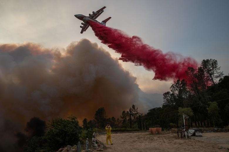 A woman wearing flame-resistant clothing photographs an airplane as it drops red fire retardant on the Glass Fire at a vineyard in Deer Park, California, U.S. September 27, 2020. REUTERS/Adrees Latif TPX IMAGES OF THE DAY
